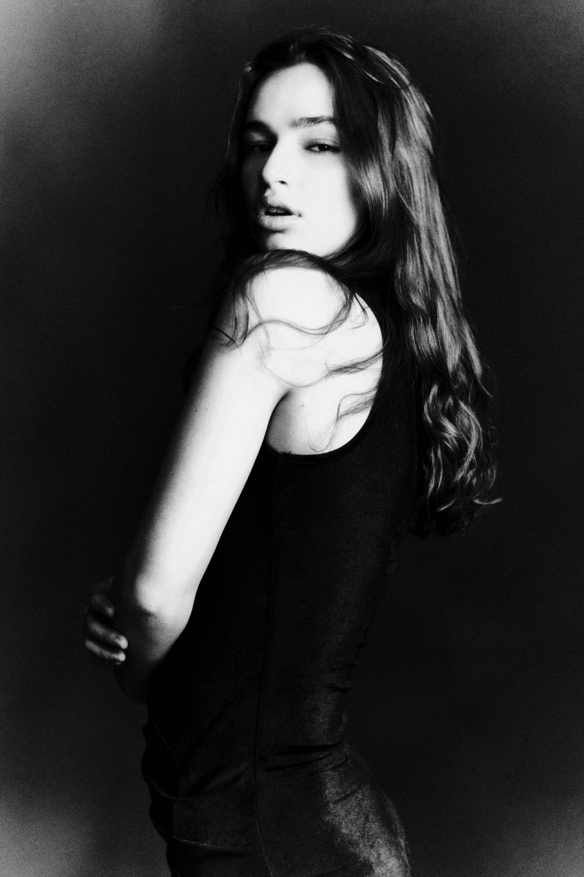 Woman with long dark hair in a black top glancing back over her shoulder, black and white portrait