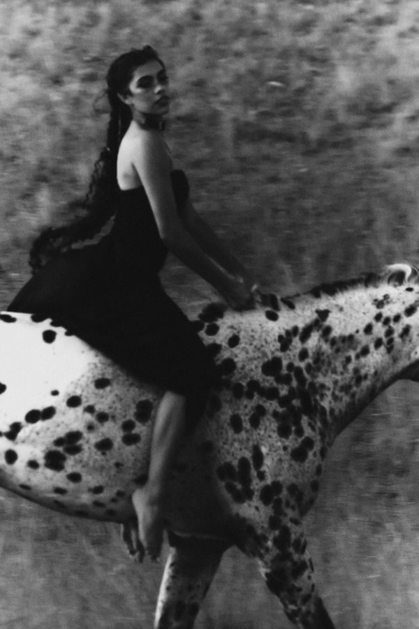 Woman in a black dress riding a spotted Appaloosa horse across a field, grainy black and white