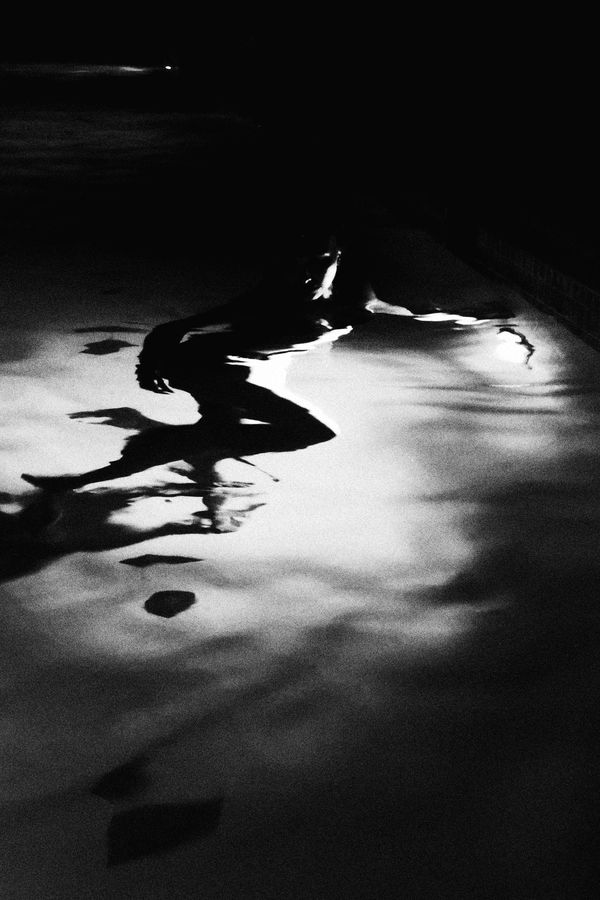 Figure floating in dark rippling water with light reflections, black and white